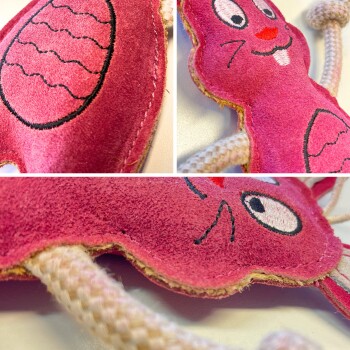 Nahaufnahme eines rosa plüschigen Katzenspielzeugs in Form eines Hasen, mit gestickten Gesichtszügen und Seilgliedern.