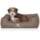 Flauschiger braun-weißer Welpe in einem braunen Hundebett mit weißem 'KNUFFELWUFF'-Logo und Hundesilhouette.