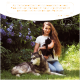 Eine Frau hält eine schwarze Katze neben einem grauen Husky, umgeben von Grün und Blumen, mit einer Sprechblase, die die Produkte von Wolfsbacher Natur lobt.