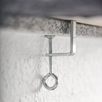 Metallhaken und Augenschraube, die an einer weißen Wand montiert sind und ein Holzregal darüber stützen.