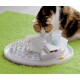 Un chat calico examine curieusement un distributeur de nourriture interactif blanc pour animaux de compagnie sur un tapis vert vif, avec des compartiments pour des friandises et des jouets.