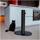 Eine schwarze Katze sitzt neben einem modernen schwarzen Kratzbaum in einer stilvollen Küche mit hellblauen Schränken und einem grauen Boden.