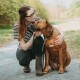 Frau in gestreiftem Hemd und Brille hockt im Freien und umarmt einen braunen Hund an der Leine mit weißer Brustzeichnung.