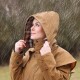 Person trägt einen braunen Regenmantel mit Kapuze im Regen und zieht die Kapuze mit beiden Händen zurecht.