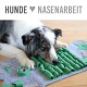 Ein Hund mit einem Merle-Fell schnüffelt und interagiert mit einer grünen Filz-Schnüffelmatte auf einem Holzboden, mit dem Text 'HUNDE ♥ NASENARBEIT' darüber.
