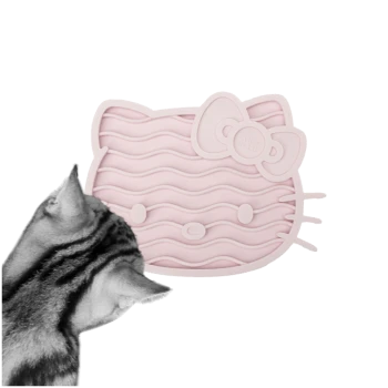 Eine graue getigerte Katze schaut neugierig auf eine rosa Silikon-Fressmatte in Katzenform mit wellenförmigen Linien und einer Schleife, beschriftet mit 'LUCY BALU.'