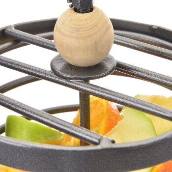 Eine Nahaufnahme eines metallenen Obsthalters mit einer Holzperle oben, gefüllt mit bunten Obstscheiben, darunter Orange und grüner Apfel.