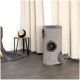 Ein gemütlicher Katzenbaum mit zwei runden Öffnungen, mit zwei grauen Katzen, die herauslugen. Eine moderne Lampe und eine drapierte Decke sind in der Nähe.