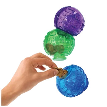 A hand is placing a dog treat into a blue KONG toy, with a green and purple KONG toy stacked above it.