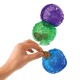 A hand is placing a dog treat into a blue KONG toy, with a green and purple KONG toy stacked above it.