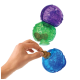 A hand is placing a dog treat into a blue KONG toy, with a green and purple KONG toy stacked above it.