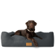 Ein brauner Hund, der auf einem stilvollen grauen Haustierbett mit lederähnlicher Textur entspannt, mit einem Holzschild beschriftet mit "FREUDENFELDER."