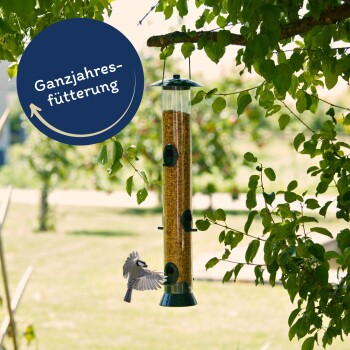 Ein mit Samen gefüllter Vogelhäuschen hängt von einem Ast, während ein kleiner Vogel sich nähert, mit "Ganzjahresfütterung" in einem kreisförmigen Design.