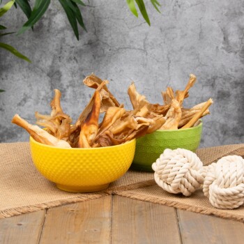 Zwei Schalen gefüllt mit getrockneten Hundeleckerlis, eine gelbe und eine grüne, auf einer Holzoberfläche mit einem Seilspielzeug daneben.