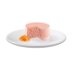 Eine runde, rosa Haustierfuttermousse mit sichtbaren orangefarbenen Karottenstücken, serviert auf einem weißen Teller mit geraspelten Karotten daneben.