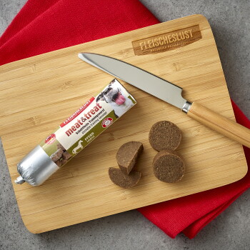 Bambus-Schneidebrett mit in Scheiben geschnittener 'meat&treat' Trainingswurst für Hunde, einem Messer und eingeprägtem 'FLEISCHESLUST'-Logo.