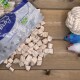 Verstreute weiße Würfel-Hundeleckerlis aus einer Plastiktüte mit der Aufschrift 'Premium Quality' auf einem Holztisch mit einem Seilball und zwei Plüschmäusen