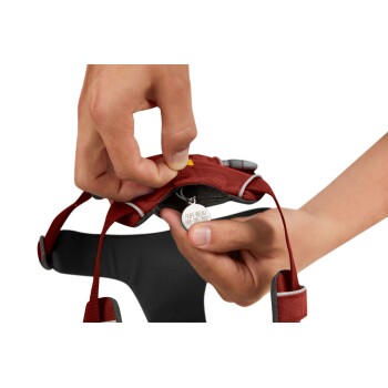 Eine Person passt ein rotes Hundegeschirr an und zeigt ein Etikett mit "RUFF WEAR" und einer Telefonnummer, das seine Merkmale hervorhebt.