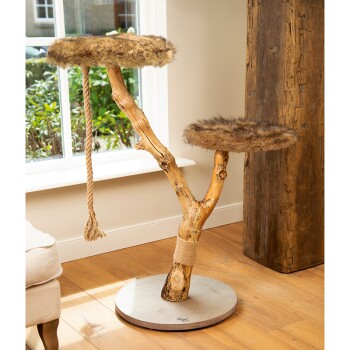 Katzenbaum aus natürlichem Holz mit zwei pelzigen Plattformen und einem Sisal-Seil zum Kratzen, in einem hellen Raum mit Holzboden.