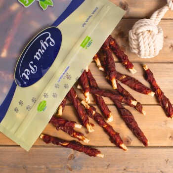 Eine Tasche mit Haustierleckereien, die mit "Furta Pet" beschriftet ist, mit dem Text "Premiumqualität" und "100% natürlich" auf einer Holzoberfläche, umgeben von gedrehten Fleischstangen.