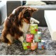 Un chien brun et blanc examine curieusement une pile de boîtes de nourriture pour animaux de compagnie colorées étiquetées "wow", présentant des saveurs comme le bœuf avec des carottes et le saumon sauvage.
