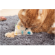 Eine orangefarbene getigerte Katze liegt auf einem grauen Teppich und knabbert verspielt an einem kleinen, gemusterten Stoffspielzeug mit bunten Fischen und Vögeln.