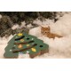 Orange tabby kitten lying in fluffy white bedding next to a green Christmas tree-shaped cat scratcher with ornaments.