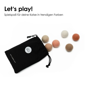 Eine fokussierte Katze spielt mit bunten Filzkugeln auf einer dunklen Oberfläche, mit dem Text "Lautloser Spielspaß dank dämpfendem Wollfilz" darüber.