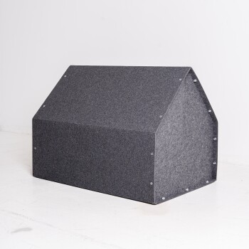 Ein graues Filzhaustier mit einem dreieckigen Dachdesign, das auf einem weißen Boden vor einem schlichten Hintergrund steht.