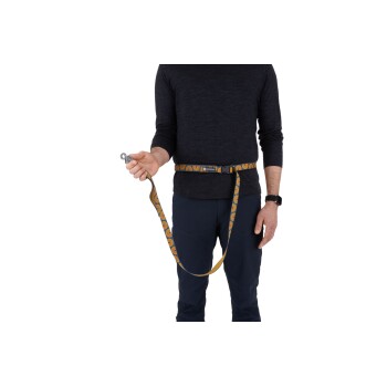 Eine Person in einem dunklen Langarmshirt hält eine Hundeleine, die an einem Gürtel befestigt ist, mit einem bunten Design.