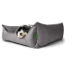 Ein kleiner schwarz-weißer Hund legt seinen Kopf auf ein gemütliches graues Hundebett mit einem grünen Etikett, das ein dezentes Hundesilhouetten-Design zeigt.