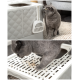 Eine graue Katze nähert sich neugierig einer modernen Katzentoilette mit einer weißen Schaufel, während eine andere graue Katze die Katzentoilette benutzt.