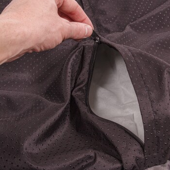 Eine Hand öffnet einen dunklen, perforierten Bezug für ein Haustierbett und zeigt ein weiches Innenfutter.