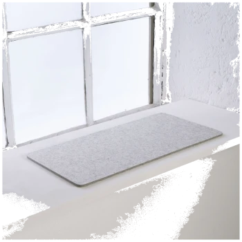 Eine graue Filz-Haustiermatte auf einer weißen Fensterbank, mit natürlichem Licht, das durch ein Fenster im Hintergrund strömt.