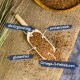 Ein Holzlöffel mit Leinsamen auf Jute, beschriftet mit "als Ergänzung," "proteinreich," "glutenfrei," und "Omega-3-Fettsäuren."