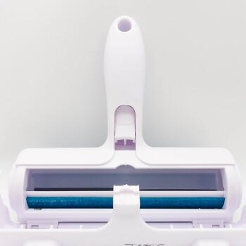 Ein weißer Tierhaareentferner mit einer blauen Rolle, ausgestattet mit einem Griff und einem Fach für einfache Reinigung.