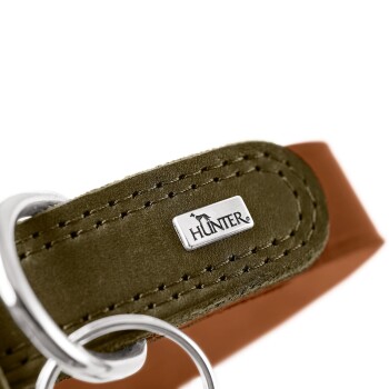 Nahaufnahme eines grünen Wildlederhalsbands mit silbernen D-Ringen und Metallanhänger mit 'HUNTER'-Logo; braunes Lederfutter sichtbar.
