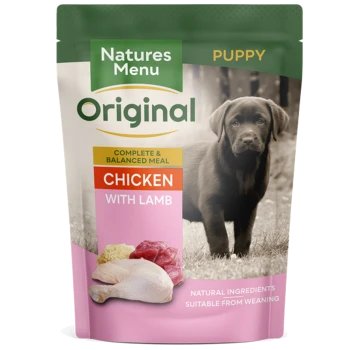 Pouch of Natures Menu Original puppy food featuring chicken with lamb, with a black Labrador puppy in the background.