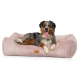 Ein Hund, der bequem auf einem plüschigen, rosa Cordbett für Haustiere liegt, mit einem kleinen braunen Etikett, das eine Hundesilhouette zeigt.