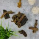 Eine Vielzahl von Hundekauartikeln in einer schwarzen Schüssel, umgeben von verschiedenen Texturen und zwei weißen Seilspielzeugen, auf einer grauen Oberfläche.