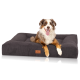 Ein glücklicher Australian Shepherd Hund liegt auf einem dunkelgrauen rechteckigen Hundebett mit einem Lederetikett, auf dem 'Knuffelwuff' steht.