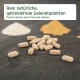 Rein natürliche, getreidefreie Gelenktabletten auf einer dunklen Oberfläche verstreut, mit weißen und gelben Pulvern im Hintergrund.