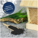 Ein hölzerner Vogelhausfütterer gefüllt mit Saatgut-Mix, umgeben von grünem Gras und einer Schaufel schwarzer Samen, mit dem Text "Ideal als Vogelfutter-Ergänzung."