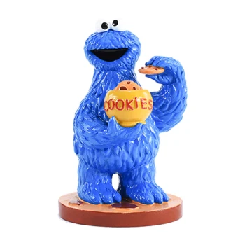 Niebieska, futrzasta postać z kreskówki trzymająca żółty słoik na ciastka z napisem "CIASTKA" i ciastko w prawej ręce, uśmiechająca się.