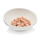Eine weiße Schüssel gefüllt mit zerriebenem rosa Katzenfutter, das Thunfisch ähnelt, vor einem schlichten Hintergrund.