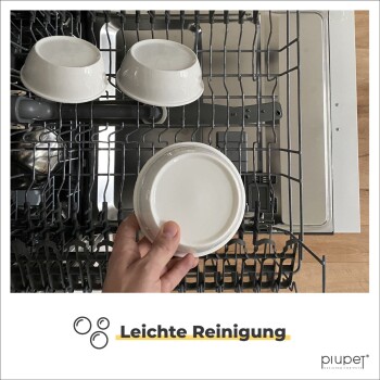 Eine Hand hält eine weiße Hundefutterschüssel über einem Geschirrspüler, mit zwei zusätzlichen Schalen, die darin platziert sind. Der Text lautet "Leichte Reinigung."