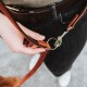 Eine Person hält eine braune Leder-Hundeleine, die sie an einen Metallclip anbringt, mit dunklen Jeans und einem braunen Gürtel sichtbar.
