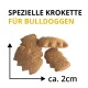 Drei braune Bulldoggen-Kroketten mit Größenpfeilen; sichtbarer Text: 'SPEZIELLE KROKETTE FÜR BULLDOGGEN' und 'ca. 2 cm'.