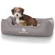 Ein kleiner, flauschiger Welpe sitzt bequem in einem grauen Hundebett mit dem Logo 'KNUFFELWUFFF', das prominent auf der Vorderseite angezeigt wird.