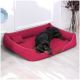 Ein schwarzer Dobermann liegt bequem auf einem lebhaft roten Hundebett mit einem kleinen Kissen, in einem stilvollen Innenraum.